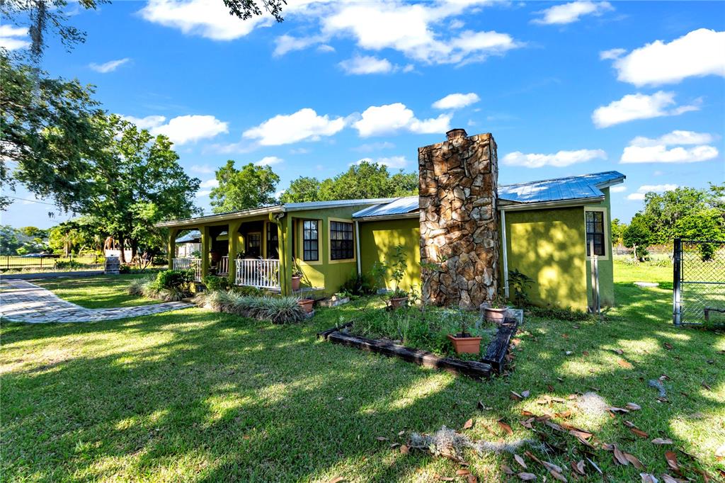 A single-story house with a stone chimney, metal roof, and a covered front porch — 13610 ACKER ROAD, DOVER, FL
