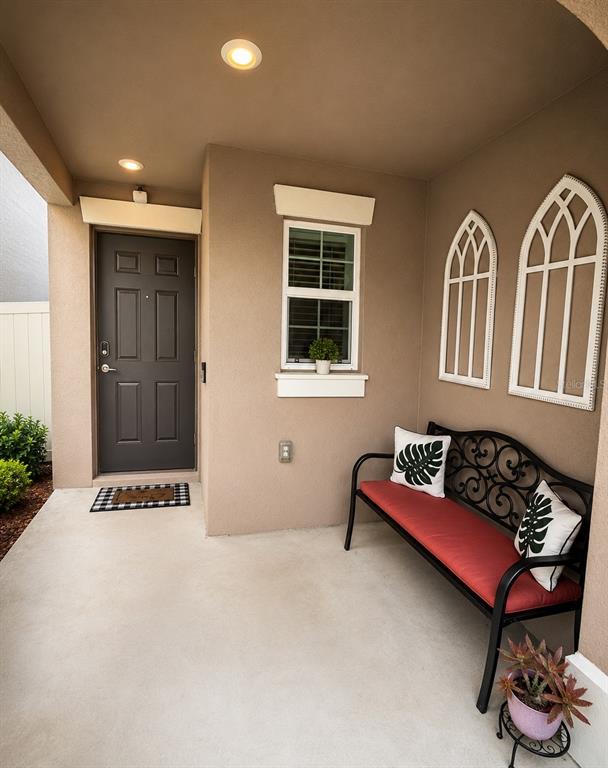 A covered front porch features a dark door, a window, and a black metal bench — 9950 BRANCHING SHIP TRACE, WESLEY CHAPEL, FL