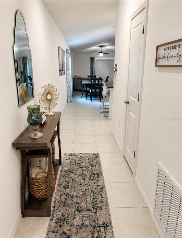 A hallway with tile flooring leads to a dining area featuring a table and chairs — 9950 BRANCHING SHIP TRACE, WESLEY CHAPEL, FL