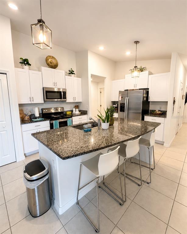 A kitchen features white cabinets, granite countertops, a central island with bar stools, and stainless-steel appliances — 9950 BRANCHING SHIP TRACE, WESLEY CHAPEL, FL