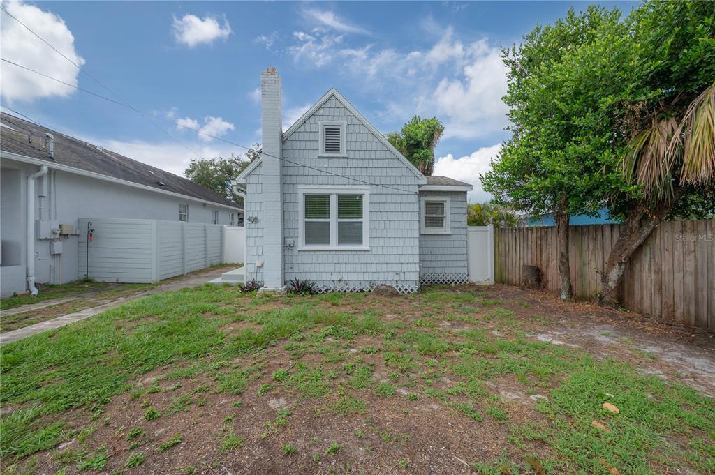 A light blue cottage with a chimney stands behind a grassy yard and wooden fence — 405 E CAYUGA STREET, TAMPA, FL