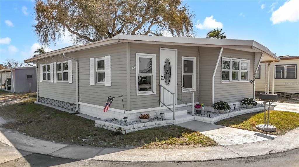 A single-story manufactured home with gray siding, white trim, and a small front porch — 10101 N LAKE DRIVE UNIT 89, LARGO, FL