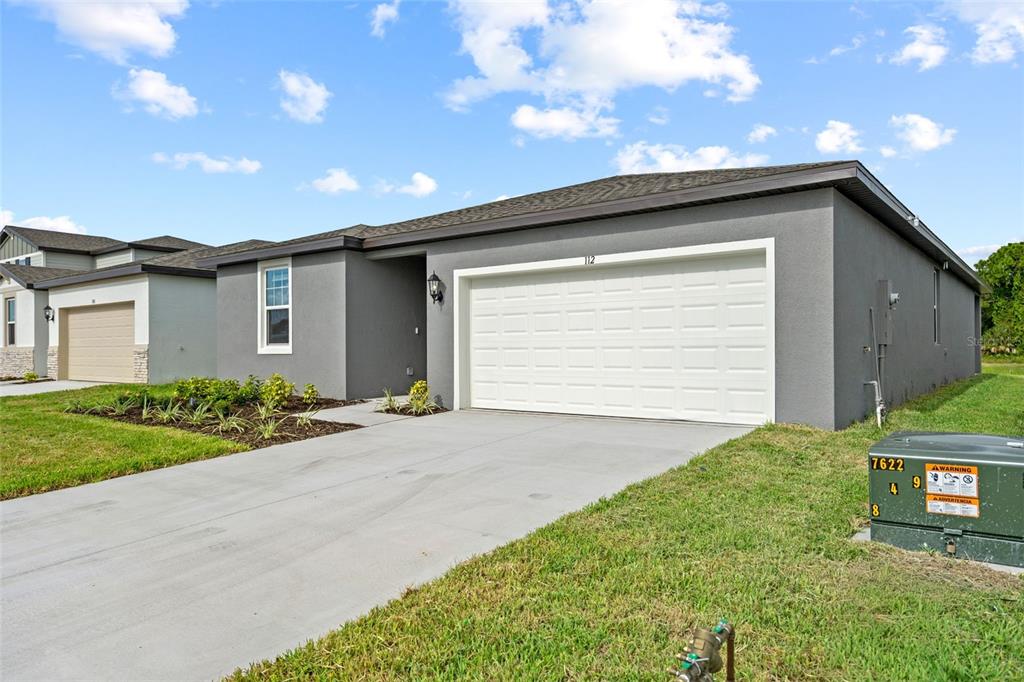 A gray single-story house features a white garage door, a concrete driveway, and landscaped beds — 112 OUTBACK HIDEAWAY AVENUE, NOKOMIS, FL