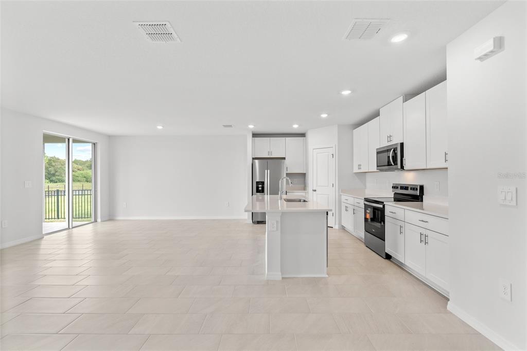 A bright, open-concept kitchen and living area featuring white cabinetry, a center island, and tile flooring — 112 OUTBACK HIDEAWAY AVENUE, NOKOMIS, FL