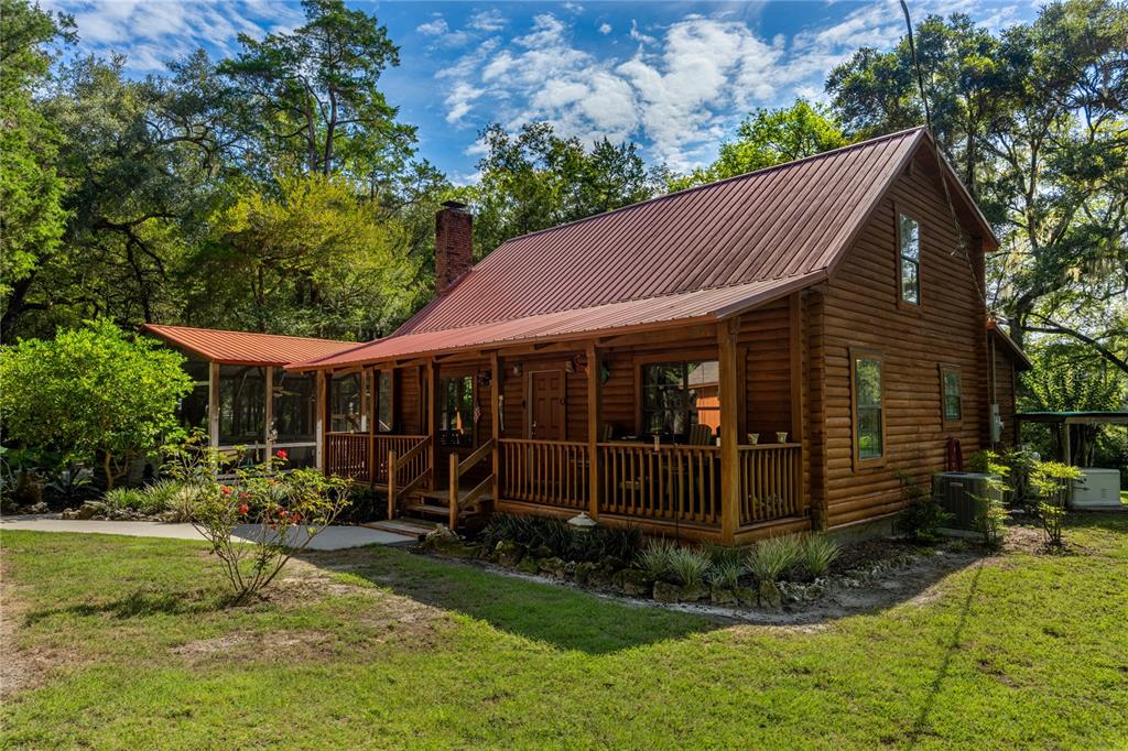 A log cabin with a metal roof and a covered front porch sits on a lawn — 16350 NE 53RD LANE, WILLISTON, FL