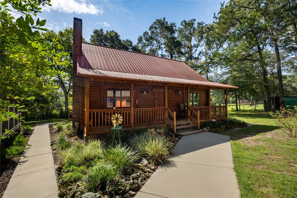 A rustic log cabin with a metal roof and a wooden porch sits in a yard — 16350 NE 53RD LANE, WILLISTON, FL