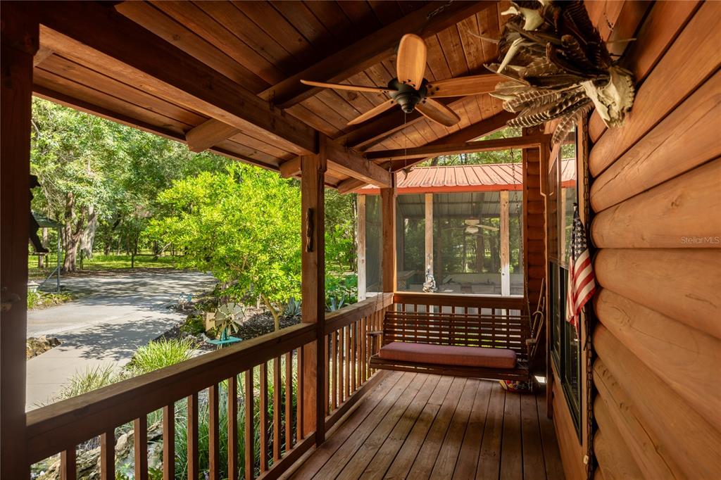 A covered wooden porch features a hanging swing, a ceiling fan, and log cabin walls — 16350 NE 53RD LANE, WILLISTON, FL