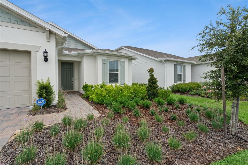 The exterior of a single-story house features a paved walkway, landscaping, and a garage — 2546 DEL WEBB DR, MINNEOLA, FL