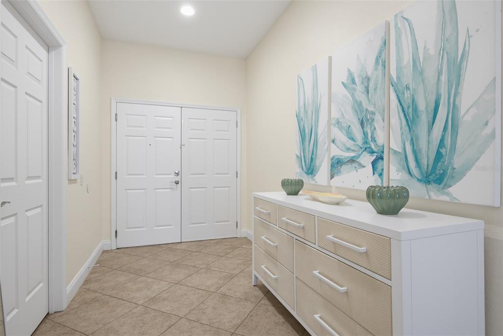 An entryway features a white dresser, wall art, and tiled flooring leading to double doors — 2 OCEANS WEST BOULEVARD UNIT 103, DAYTONA BEACH SHORES, FL