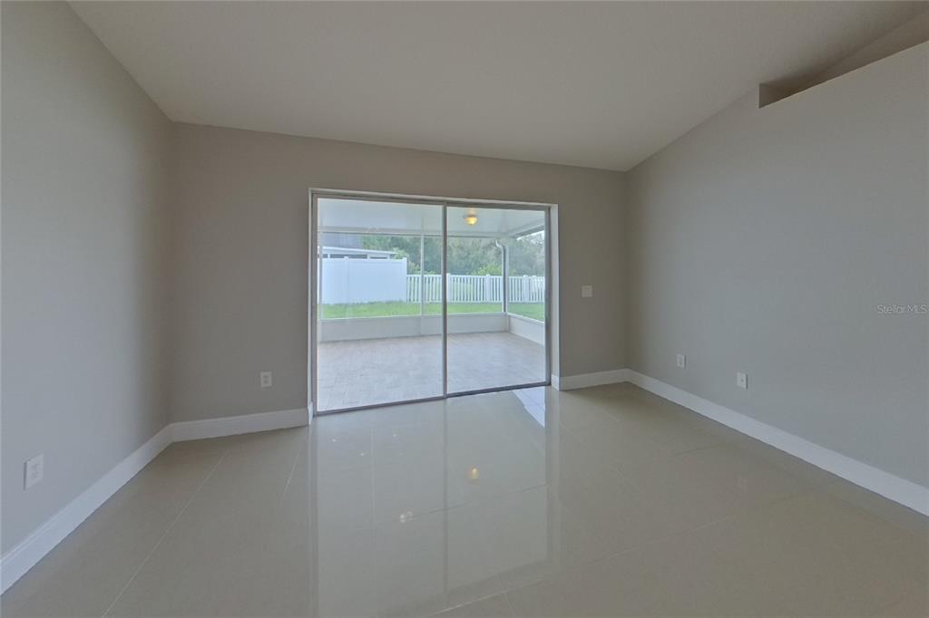 An empty room with light-colored tile flooring and sliding glass doors leading to a patio — 30746 BIRDHOUSE DRIVE, WESLEY CHAPEL, FL