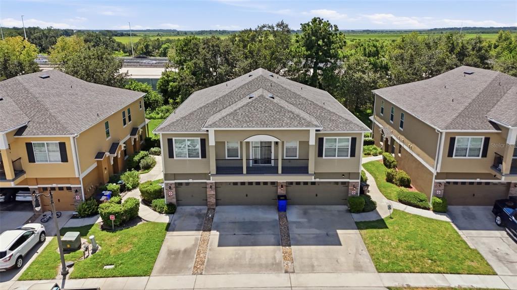 An aerial view shows three multi-story townhomes with attached garages and driveways — 2276 BETSY ROSS LANE UNIT A, ST CLOUD, FL