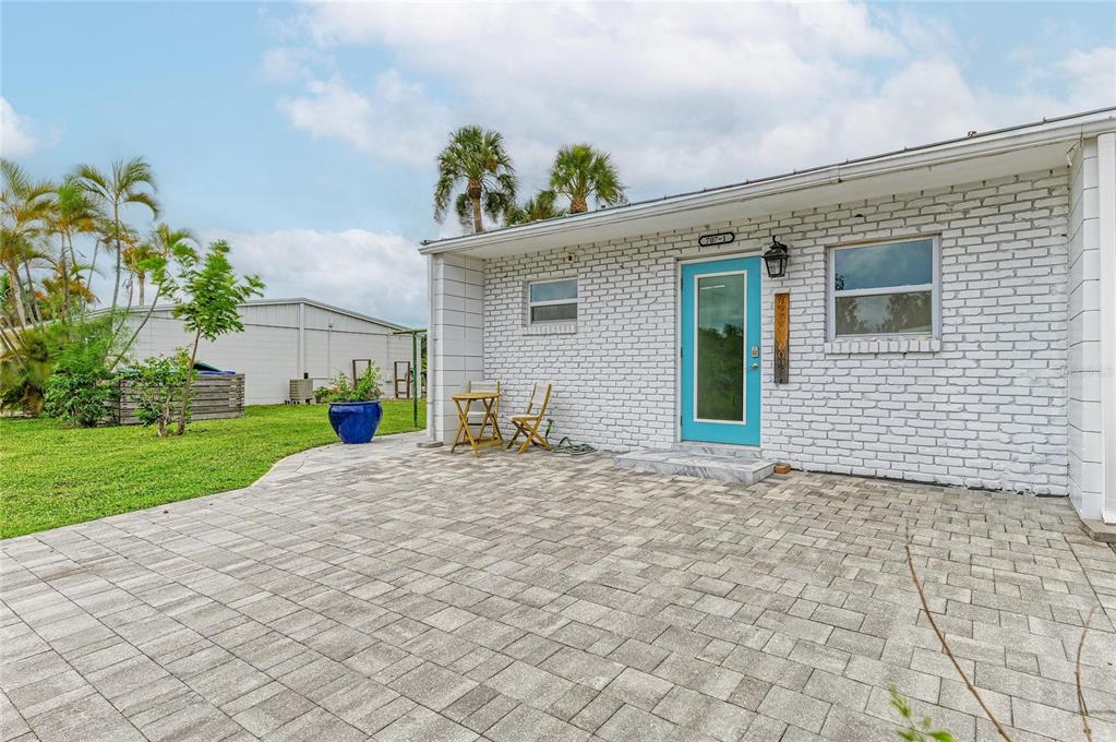 A white brick exterior wall features a bright blue door and a paved patio area — 707 SAINT JUDES DRIVE S UNIT 1, LONGBOAT KEY, FL