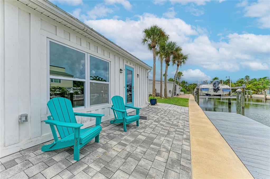 Two turquoise Adirondack chairs sit on a paved patio beside a canal with a boat — 707 SAINT JUDES DRIVE S UNIT 1, LONGBOAT KEY, FL
