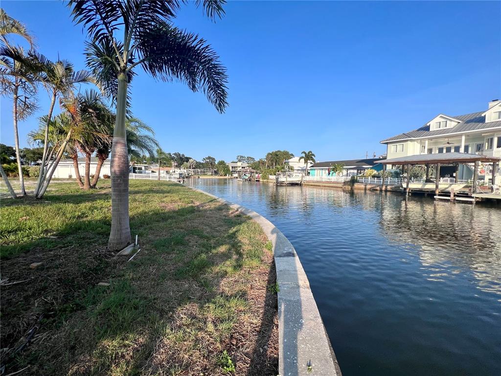 A canal view features a grassy yard, palm trees, and waterfront homes with boat docks — 1796 BROOKSIDE BOULEVARD, LARGO, FL