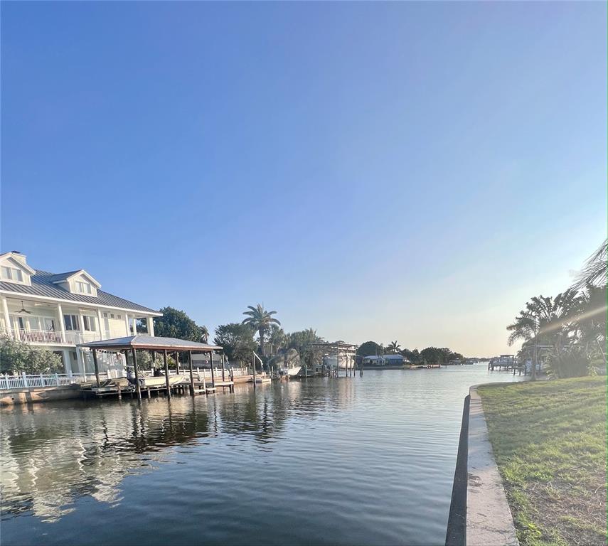 A white multi-story house with a boat dock sits along a canal under clear skies — 1796 BROOKSIDE BOULEVARD, LARGO, FL