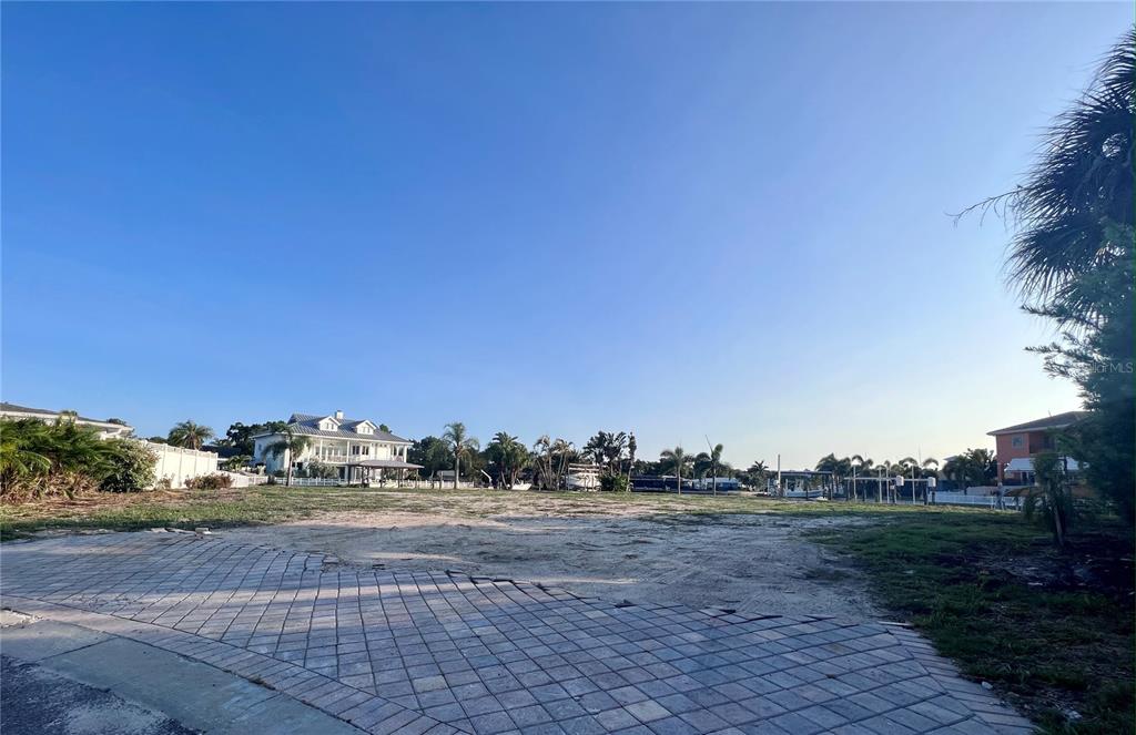 A vacant, sandy waterfront lot features a paved driveway in the foreground and surrounding homes — 1796 BROOKSIDE BOULEVARD, LARGO, FL