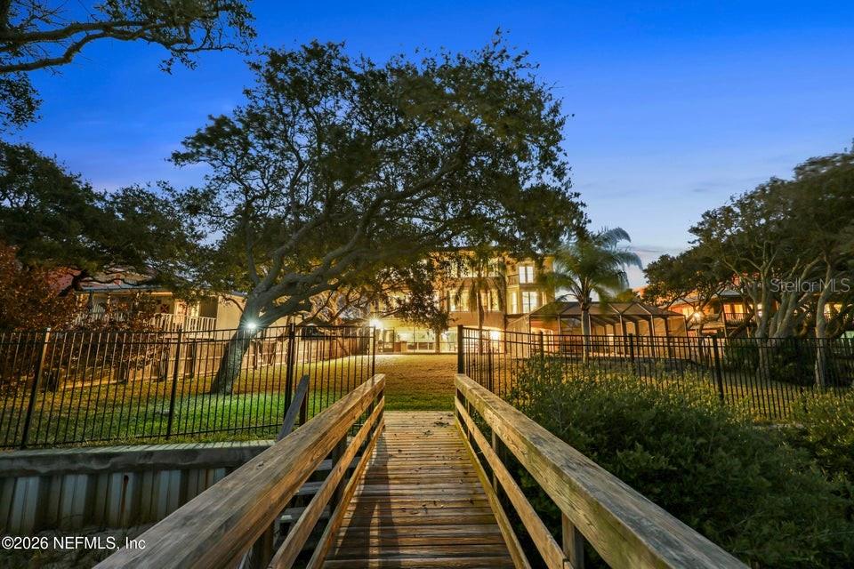 A wooden dock leads toward the backyard of a multi-story house with a fenced lawn — 7149 MIDDLETON AVENUE, ST AUGUSTINE, FL
