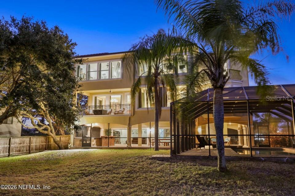 A three-story house with a screened-in pool area and a large backyard at dusk — 7149 MIDDLETON AVENUE, ST AUGUSTINE, FL
