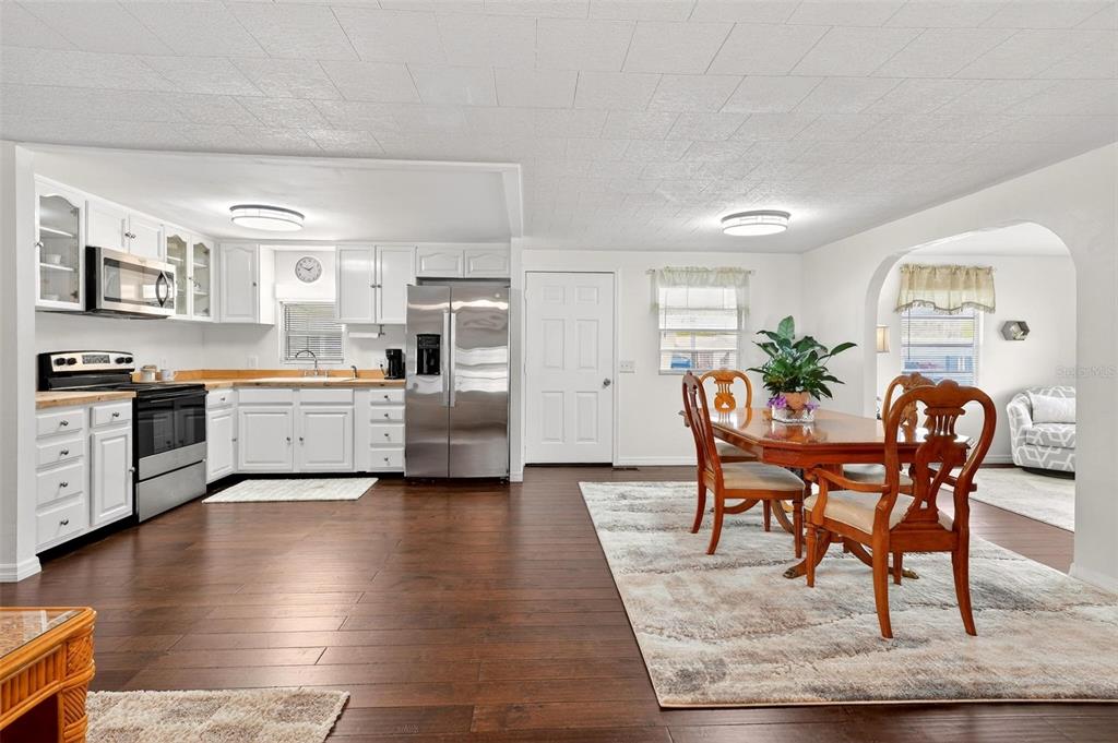 An open-concept kitchen and dining area with white cabinets, stainless appliances, and dark wood flooring — 7 COCOS PLUMOSA DRIVE UNIT A, EUSTIS, FL