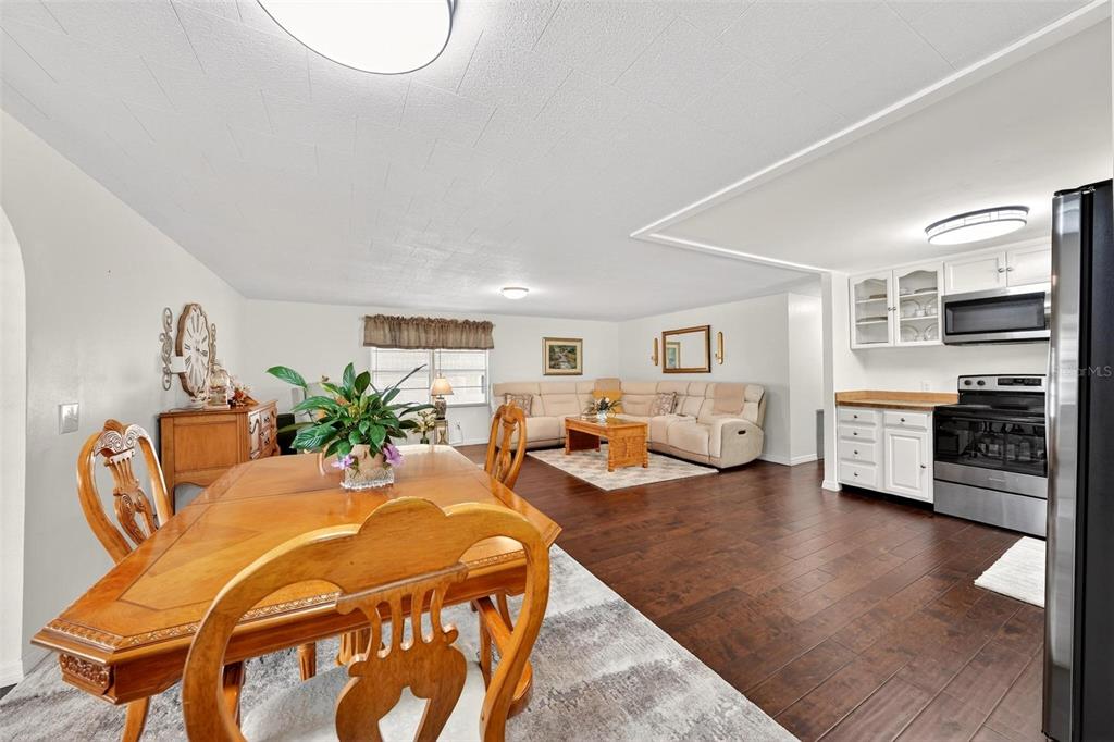 An open-concept dining and living area features wood flooring, white cabinetry, and a sectional sofa — 7 COCOS PLUMOSA DRIVE UNIT A, EUSTIS, FL