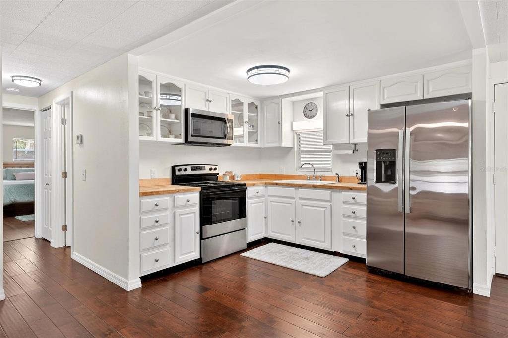 A kitchen with white cabinets, stainless steel appliances, and wood countertops on a hardwood floor — 7 COCOS PLUMOSA DRIVE UNIT A, EUSTIS, FL