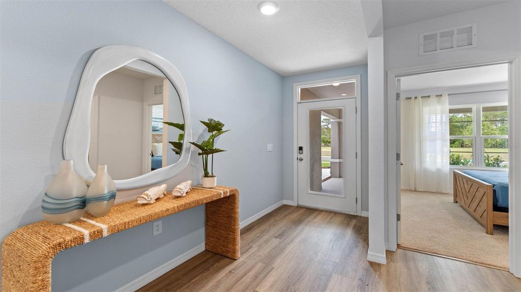 An entryway features a woven console table, an organic-shaped mirror, and a view into a bedroom — 3198 GREY MOSS DRIVE, ST CLOUD, FL