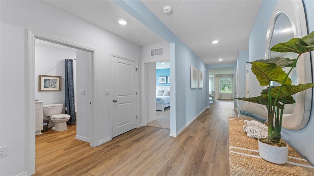 A hallway with light blue walls, wood-look flooring, and doorways leading to a bathroom and bedroom — 3198 GREY MOSS DRIVE, ST CLOUD, FL