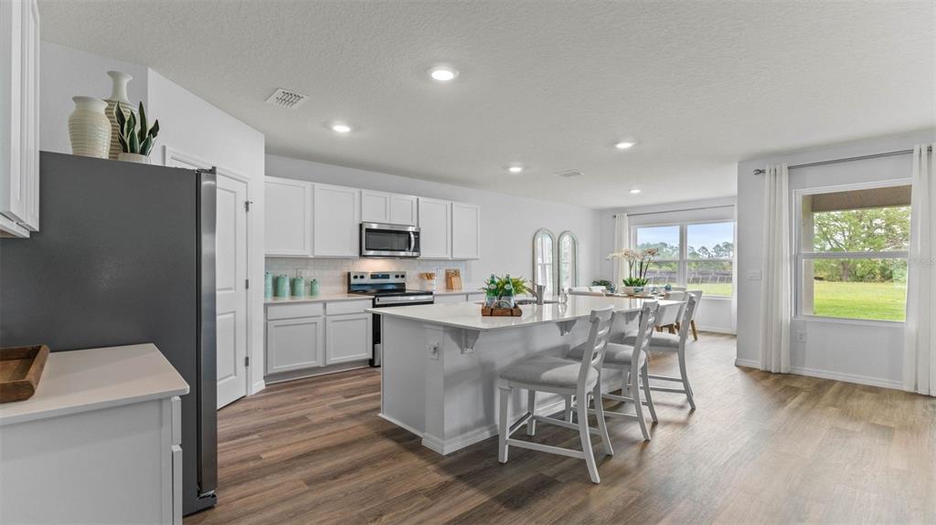 A bright kitchen features white cabinets, a large island with seating, and wood-look flooring — 3198 GREY MOSS DRIVE, ST CLOUD, FL