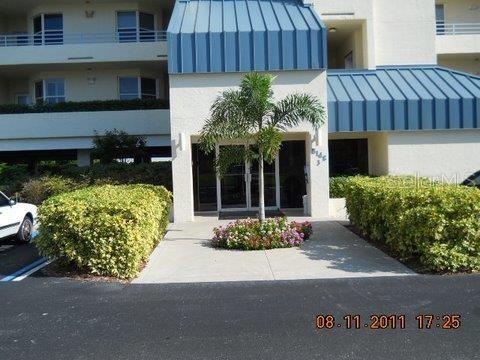 A palm tree stands in front of the glass entrance to a multi-story apartment building — 7882 SAILBOAT KEY BOULEVARD S UNIT 405, SOUTH PASADENA, FL