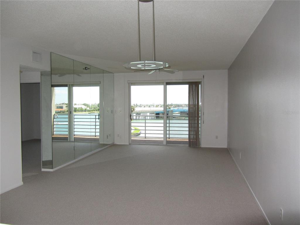 A living room with beige carpet, mirrored walls, a ceiling fan, and a balcony overlooking water — 7882 SAILBOAT KEY BOULEVARD S UNIT 405, SOUTH PASADENA, FL