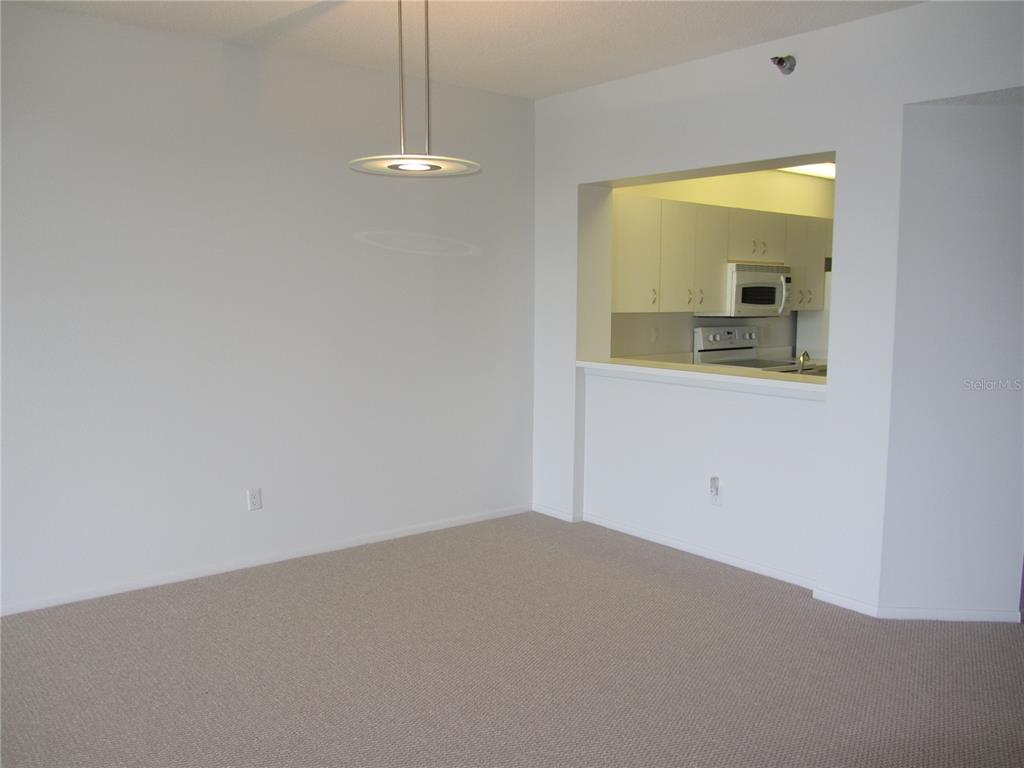 An empty dining area with beige carpet features a modern pendant light and a kitchen pass-through — 7882 SAILBOAT KEY BOULEVARD S UNIT 405, SOUTH PASADENA, FL