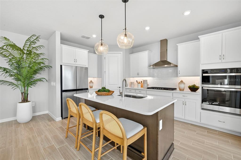 A modern kitchen features a dark wood island, white cabinetry, stainless steel appliances, and pendant lighting — 13153 OXEYE LANE, PARRISH, FL