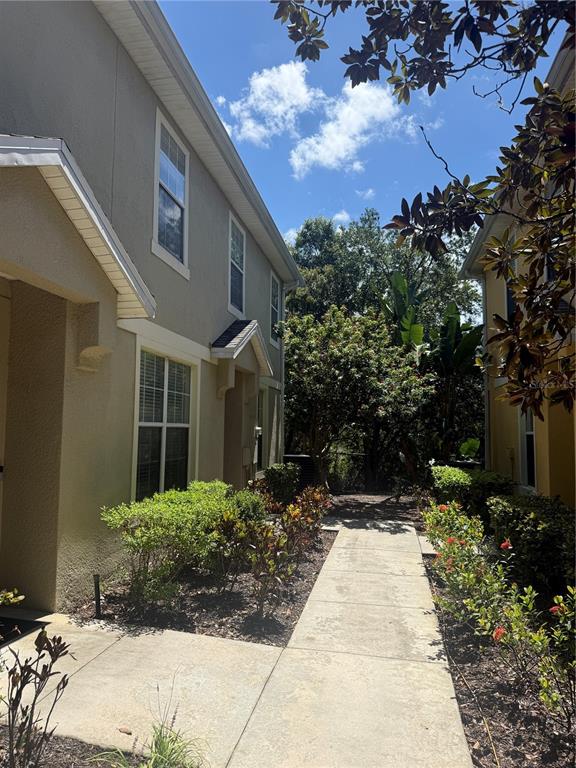 A concrete walkway leads between two multi-story residential buildings with landscaped shrubs and trees — 6730 EAGLE FEATHER DRIVE, RIVERVIEW, FL