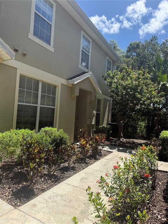 A beige two-story house exterior features a concrete walkway leading to a recessed front entrance — 6730 EAGLE FEATHER DRIVE, RIVERVIEW, FL