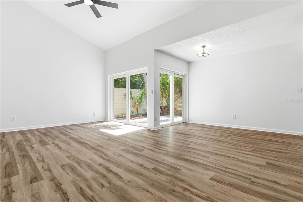An empty living room features light wood-look flooring, vaulted ceilings, and sliding glass patio doors — 2628 CEDAR VIEW COURT, CLEARWATER, FL