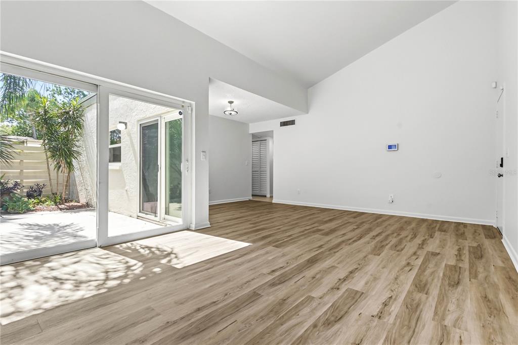 A bright living room features light wood-look flooring, vaulted ceilings, and a sliding glass door — 2628 CEDAR VIEW COURT, CLEARWATER, FL