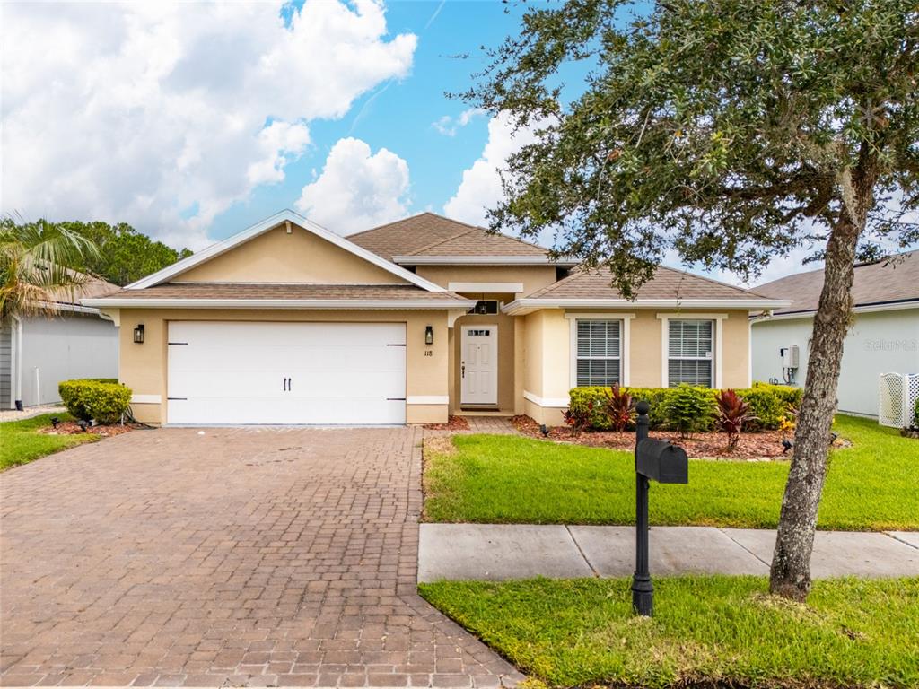 A single-story house with a white garage door, tan stucco exterior, and a brick driveway — 118 GOLFVIEW COURT, BUNNELL, FL
