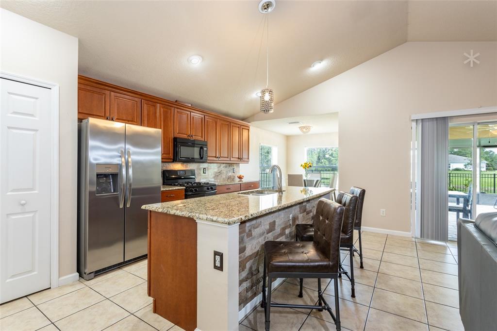 A kitchen features wood cabinets, granite countertops, a stone-faced island, and stainless steel appliances — 118 GOLFVIEW COURT, BUNNELL, FL