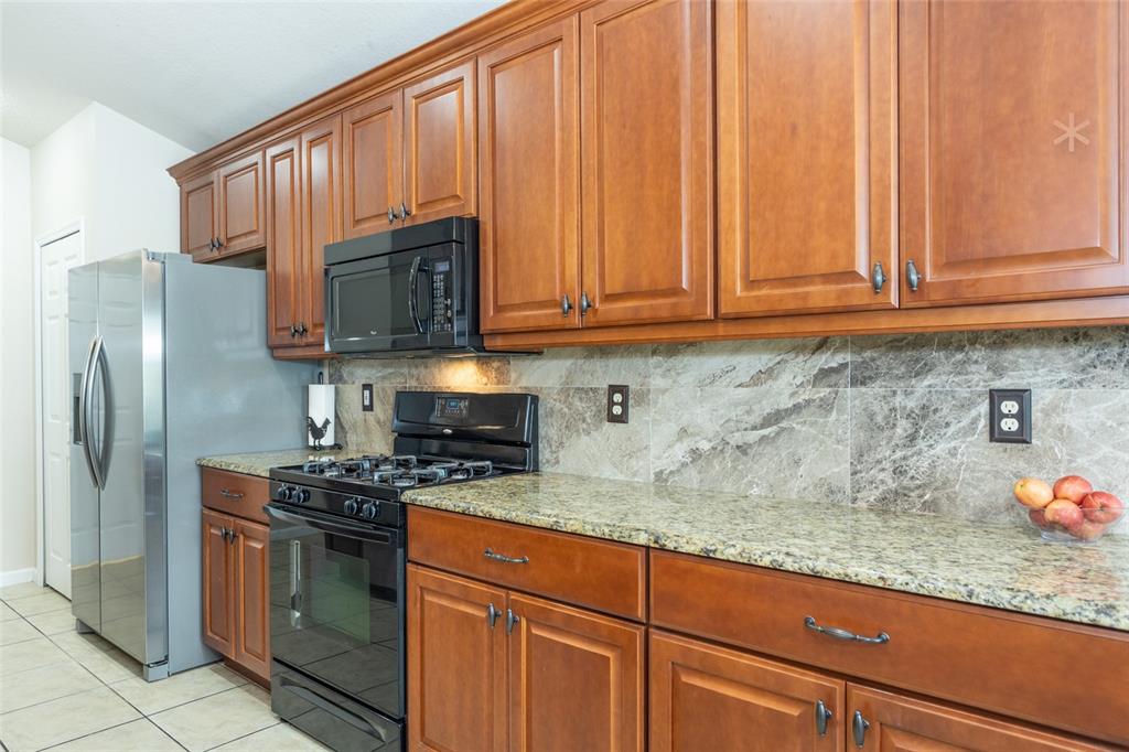 A kitchen features wood cabinets, granite countertops, a stone backsplash, and black appliances — 118 GOLFVIEW COURT, BUNNELL, FL