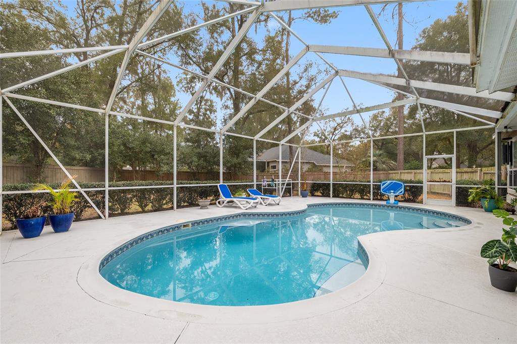 A screened-in swimming pool with lounge chairs on a concrete patio in a backyard — 9350 SW 46TH PLACE, GAINESVILLE, FL