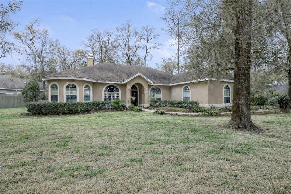 A single-story tan stucco house with arched windows sits on a large, grassy lot — 9350 SW 46TH PLACE, GAINESVILLE, FL