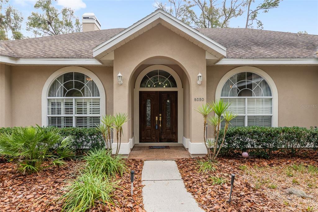 The exterior of a single-story house features a tan stucco facade, arched windows, and double doors — 9350 SW 46TH PLACE, GAINESVILLE, FL