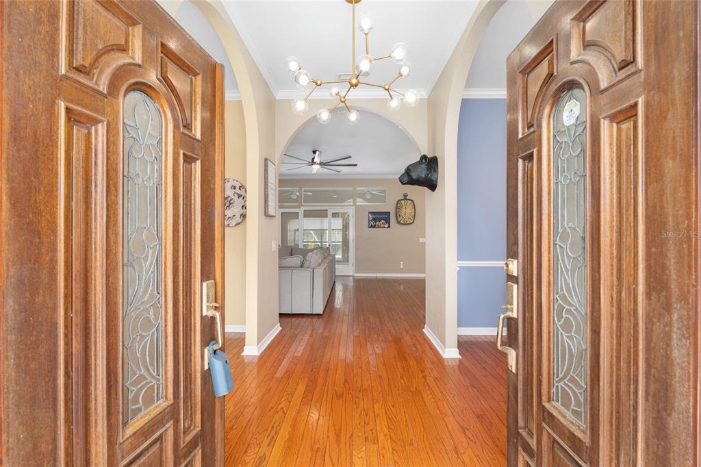A view through double wooden front doors into a foyer with hardwood floors and arches — 9350 SW 46TH PLACE, GAINESVILLE, FL