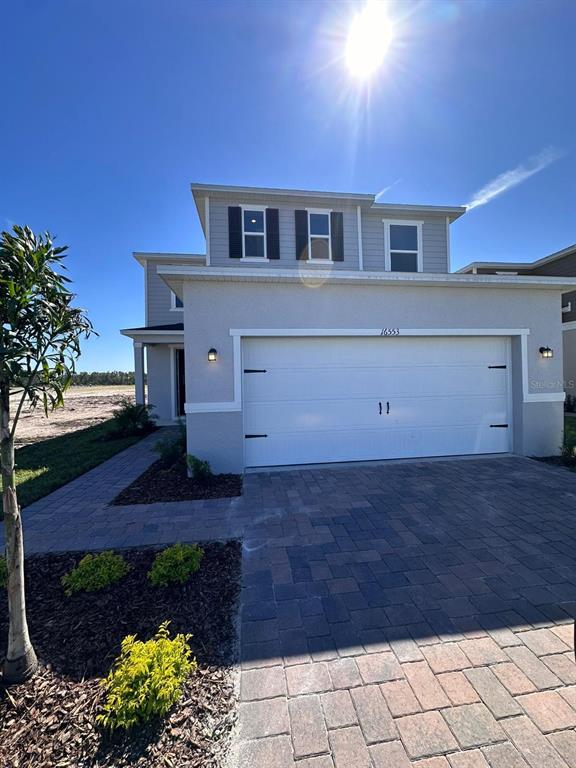A two-story house exterior features a white garage door, light-colored stucco, and a paved driveway — 16553 BROOK ISLE WAY, CLERMONT, FL