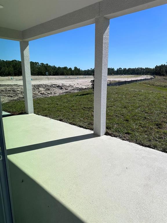 A covered concrete patio overlooks a grassy yard and an adjacent area under construction — 16553 BROOK ISLE WAY, CLERMONT, FL
