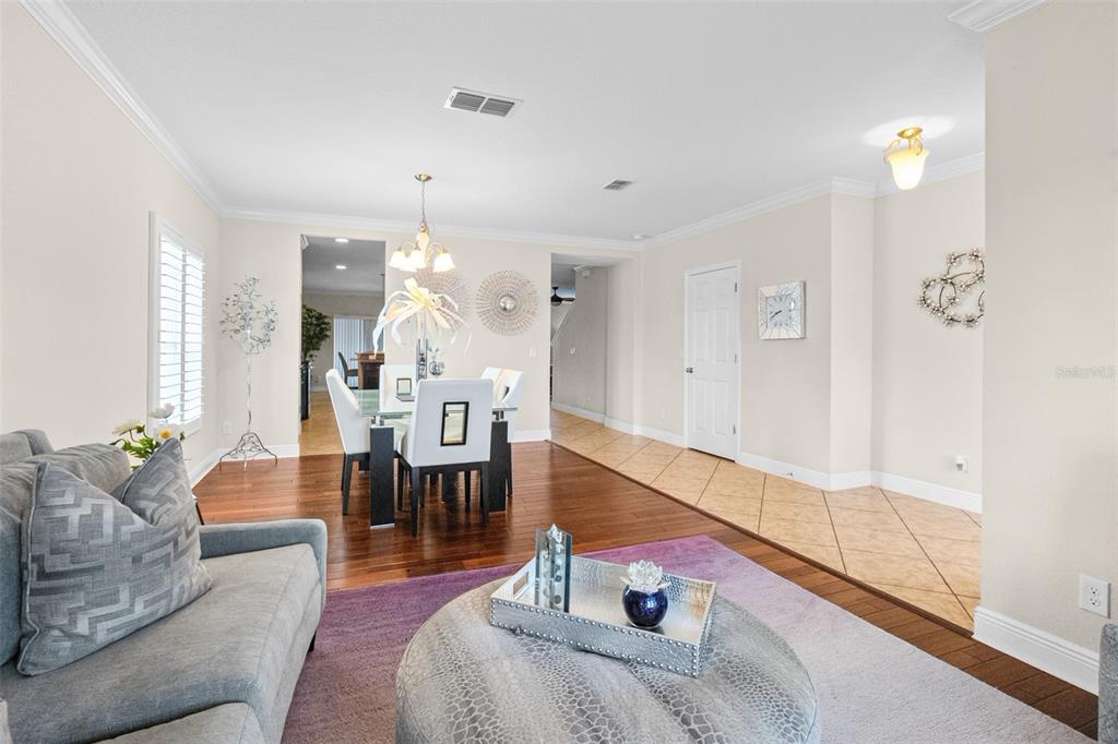 A living room with a purple rug and ottoman leads to a dining area with hardwood floors — 301 SPARROW HAWK DRIVE, GROVELAND, FL