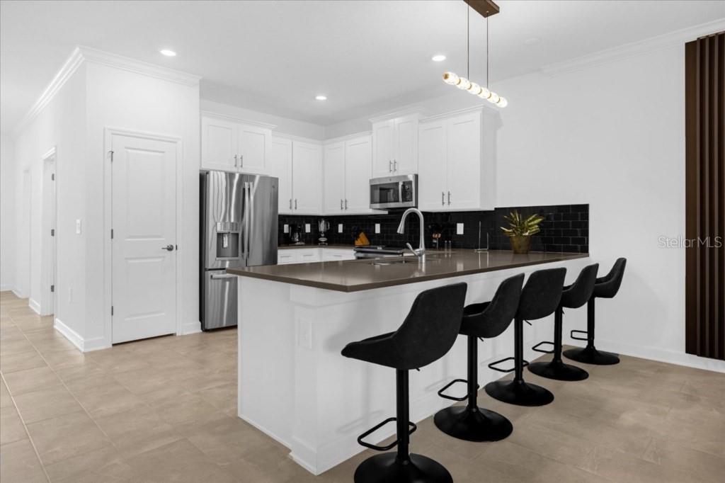 A modern kitchen features white cabinets, a dark island countertop, and four black bar stools — 2992 PENELOPE LOOP, KISSIMMEE, FL