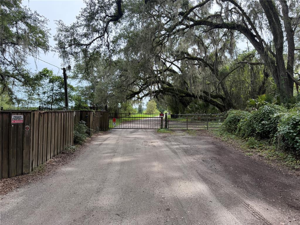 A dirt road leads to a gated entrance flanked by a wooden fence and large trees — TBD SW 89TH STREET, GAINESVILLE, FL