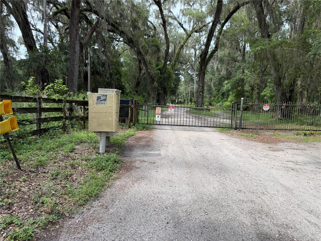 A dirt driveway leads to a gated entrance flanked by a wooden fence and mailbox — TBD SW 89TH STREET, GAINESVILLE, FL