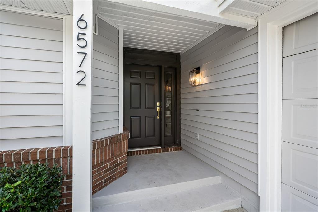 The exterior entrance features a dark door, light gray siding, and a brick base — 6572 ABERCROMBIE COURT, ORLANDO, FL